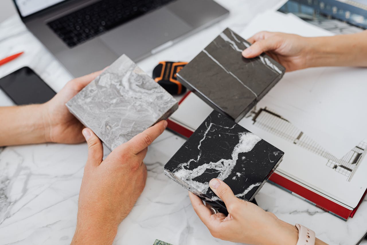Two architects selecting marble tile samples on a desk in an office setting.